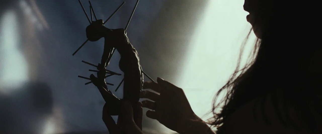 The Night House (2020) movie still: closeup — A dimly lit workspace shows a person silhouetted against a bright white background. They carefully…