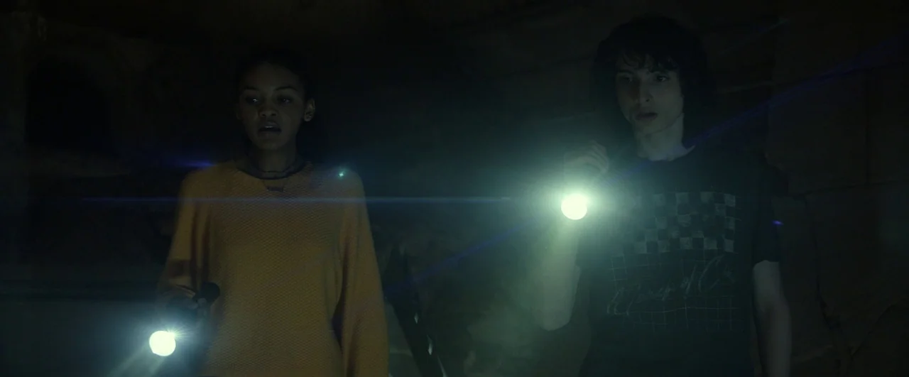 Ghostbusters: Afterlife (2021) movie still: medium — A dark, unfinished space with rough textures and deep shadows. Two teenagers stand side by side…