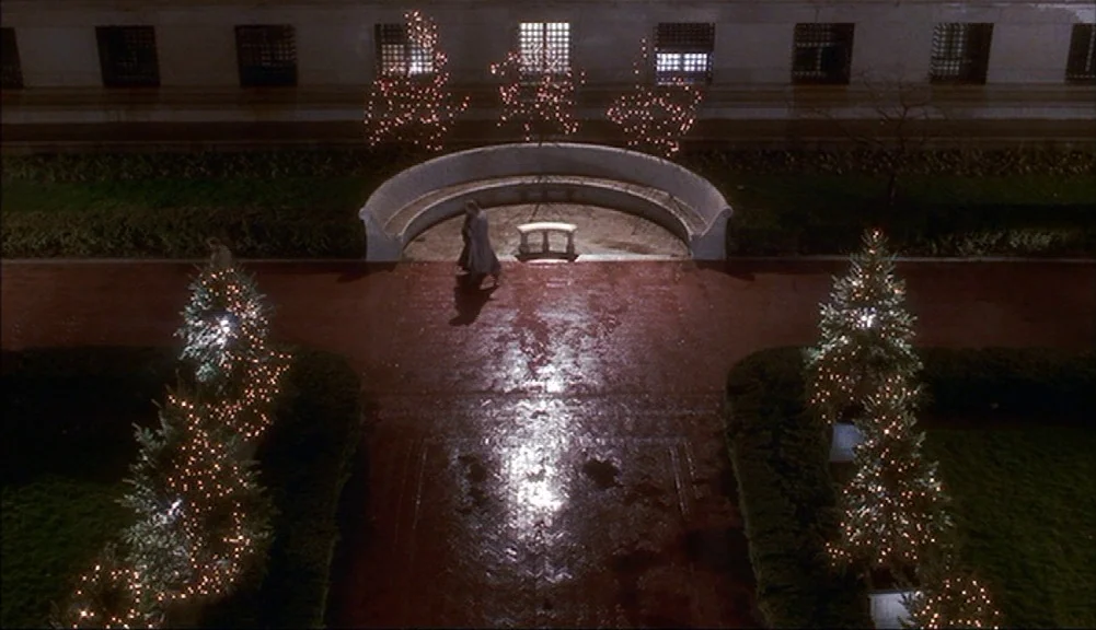 The Mirror Has Two Faces (1996) movie still: wide — A night courtyard features a curved stone bench backed by decorative string lights on trees. Two…