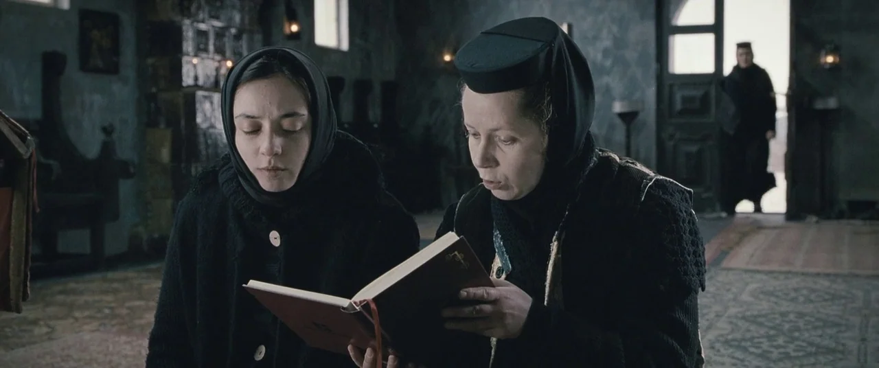 Beyond the Hills (2012) movie still: medium — A stone-walled interior space with dark furniture and a doorway leading outside. Two women in…