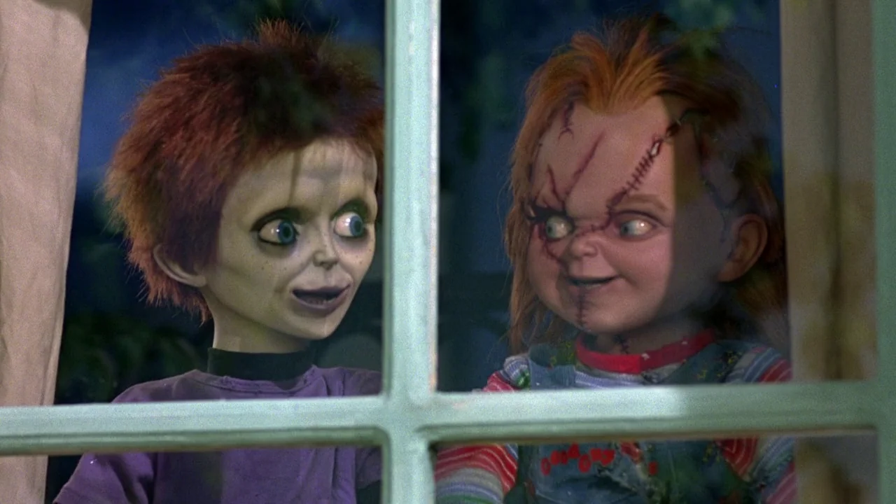 Seed of Chucky (2004) movie still: medium — Two doll characters stand side-by-side looking through a windowpane at night. The characters are framed…