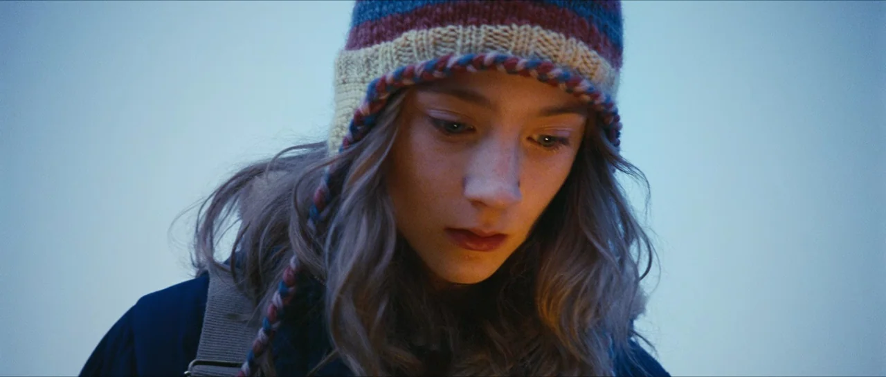 The Lovely Bones (2009) movie still: closeup — A teenage girl stands against a light blue, overcast sky. She looks downward while wearing a…