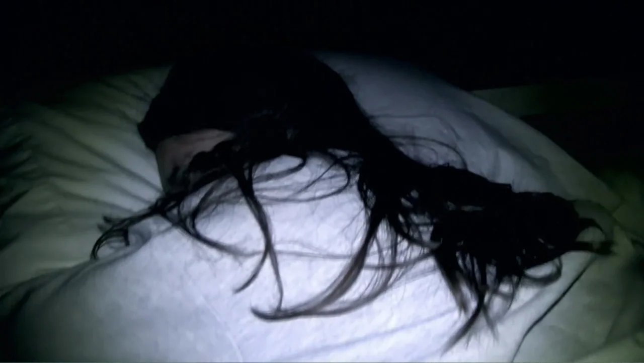 S-V/H/S: Un cortometraje de Las Crónicas del Miedo (2023) movie still: closeup — A person rests on a white pillow in a dark bedroom at night. The…