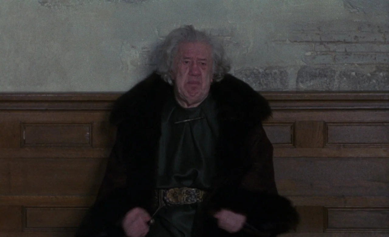Blanche (1971) movie still: medium — An interior space with a wood-paneled wall below a textured, light-colored plaster section. An elderly man with…