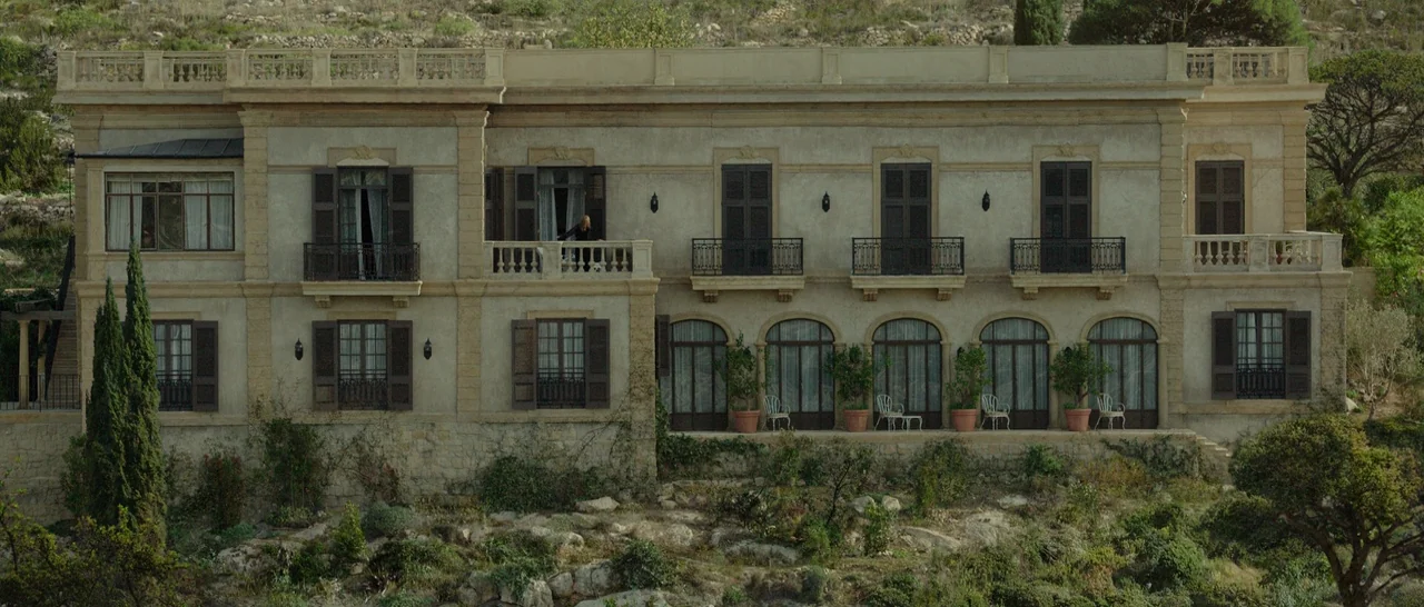 By The Sea (2015) movie still: establishing — A two-story Mediterranean-style stone mansion features multiple balconies and dark wooden shutters.…