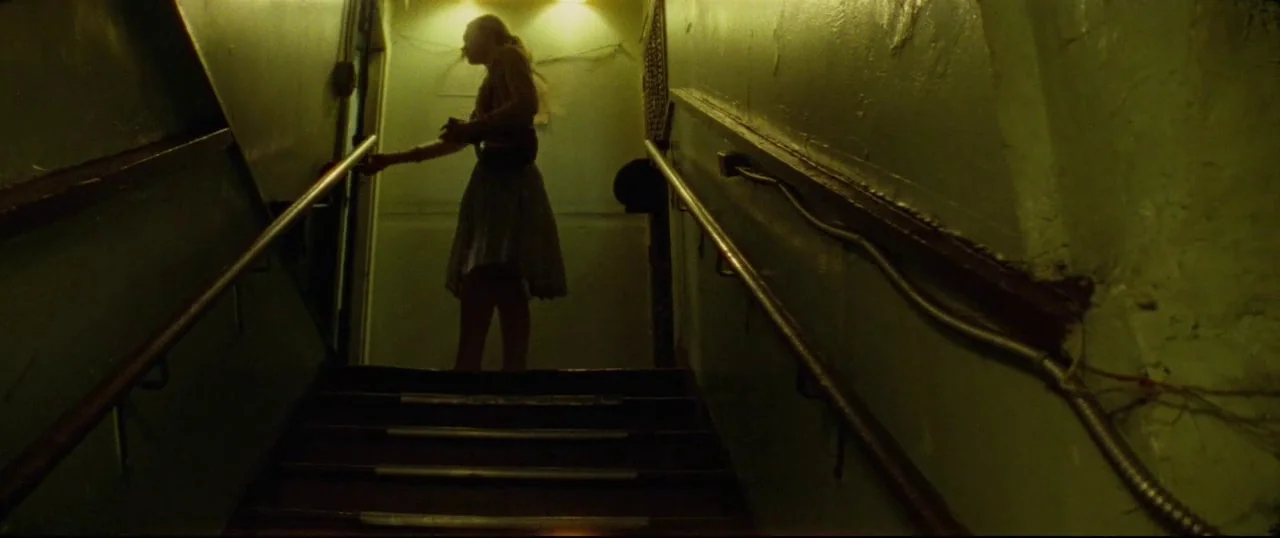 Low Down (2014) movie still: fullbody — A narrow dimly lit concrete stairwell features metal handrails and rough textured walls. A young woman…