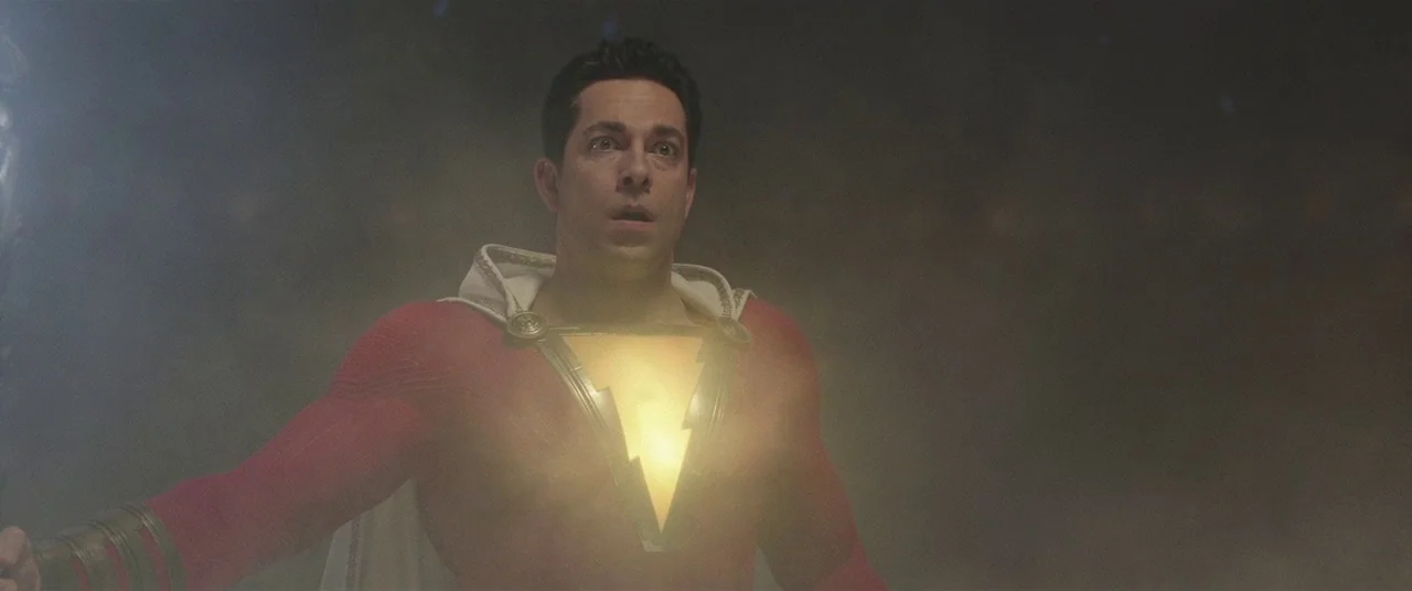 Shazam! (2019) movie still: medium — A dark, atmospheric void filled with dust particles surrounding a central figure. A man in a red suit stands…