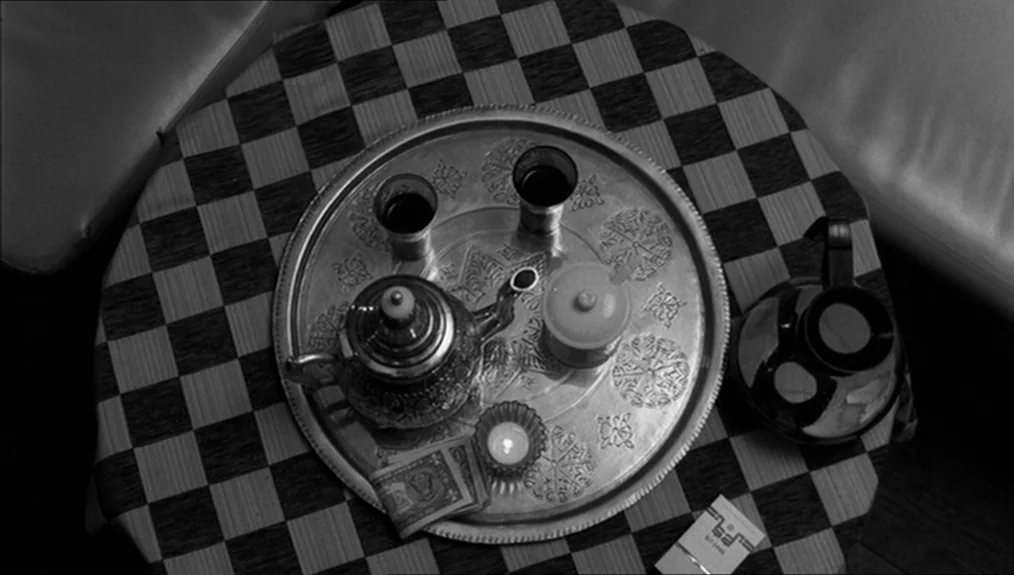 Coffee and Cigarettes (2003) movie still: closeup — A checkered tablecloth covers a round surface holding a metal tray with tea items. A small…
