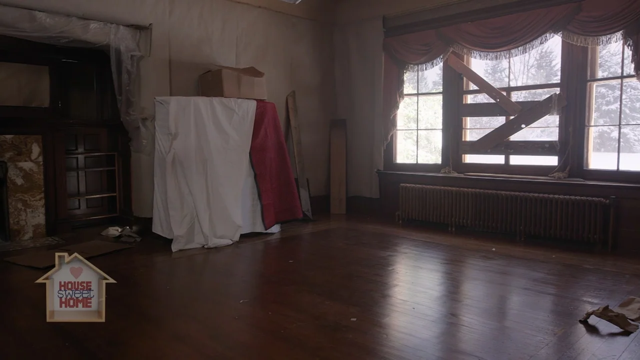 Designing Christmas (2022) movie still: establishing — A dimly lit room with dark hardwood floors and walls covered in blank wallpaper. Wooden…