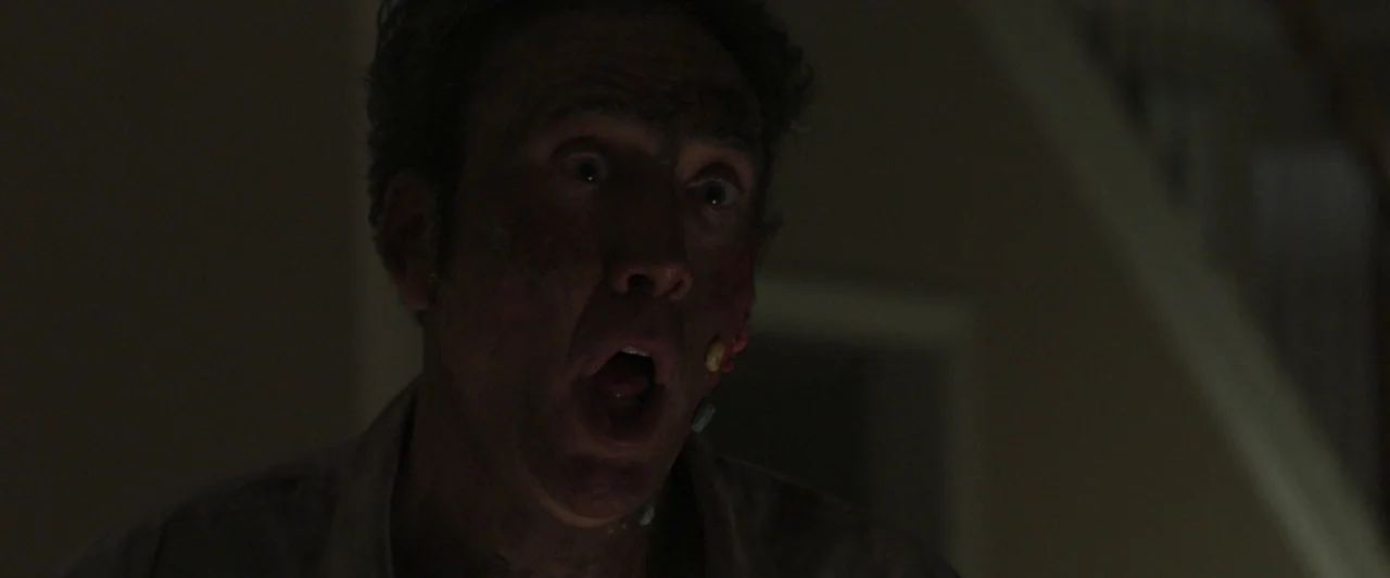 Mom and Dad (2017) movie still: closeup — A man stands in a dimly lit, largely obscured interior space. He gazes forward with a wide-eyed expression…
