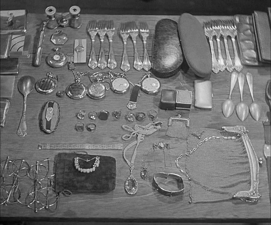 M (1931) movie still: wide — A wooden table is covered with a collection of personal belongings and jewelry items. Several antique watches,…
