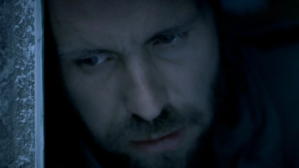 Dead Man’s Shoes (2004) movie still: closeup — A dimly lit, narrow space features a man leaning his head against a wall. The man's face is…