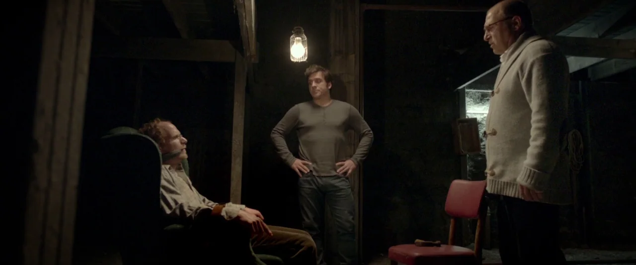 Big Bad Wolves (2013) movie still: medium — A dark, dimly lit basement features wooden ceiling joists and rough walls. Three men stand in the space,…