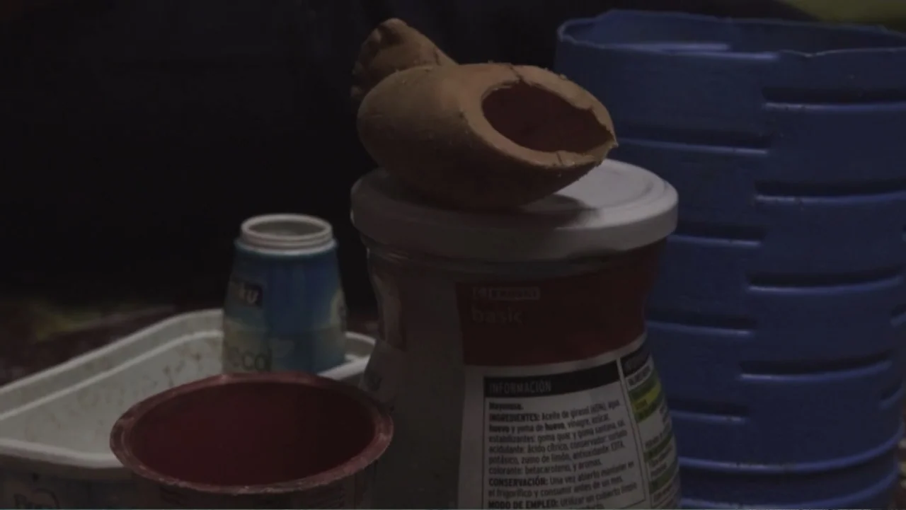 Hondar 2050 (2018) movie still: closeup — A cluttered surface features several plastic food containers and a discarded ceramic fragment. These…