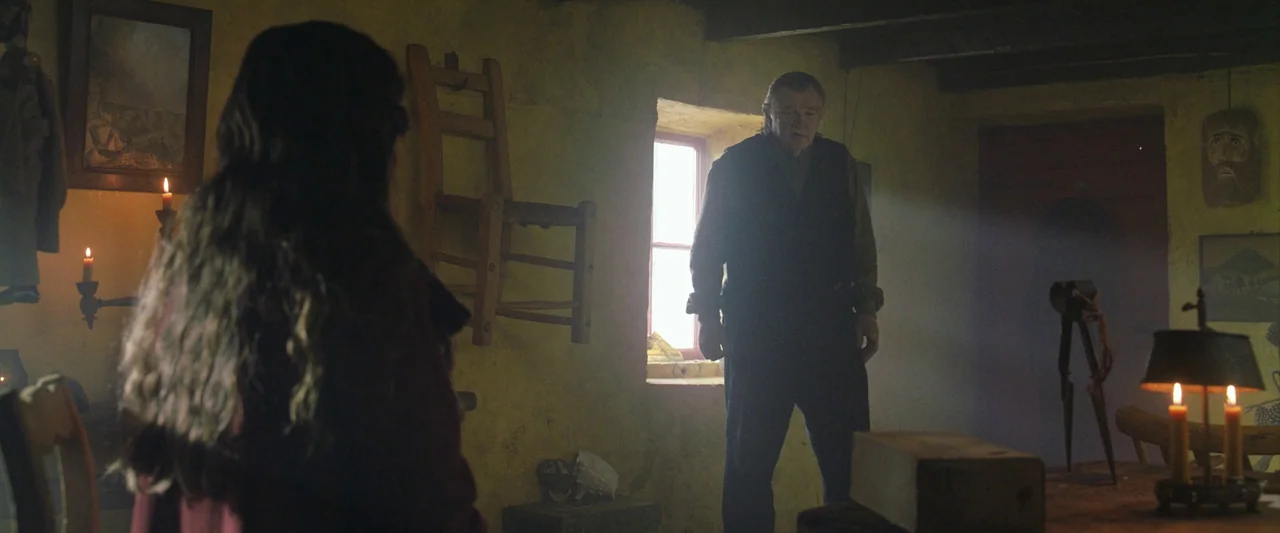 The Banshees of Inisherin (2022) movie still: medium — A rustic cottage interior features yellow plaster walls, exposed wooden beams, and antique…