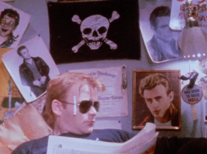 Scorpio Rising (1963) movie still: medium — A wall covered in posters including a skull and crossbones and James Dean imagery. A young man wearing…