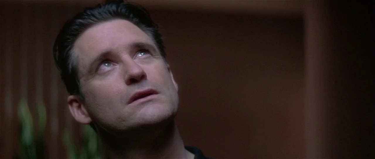 Lost Highway (1997) movie still: closeup — A dimly lit interior room with dark, indistinct background walls. A man tilts his head upward while…