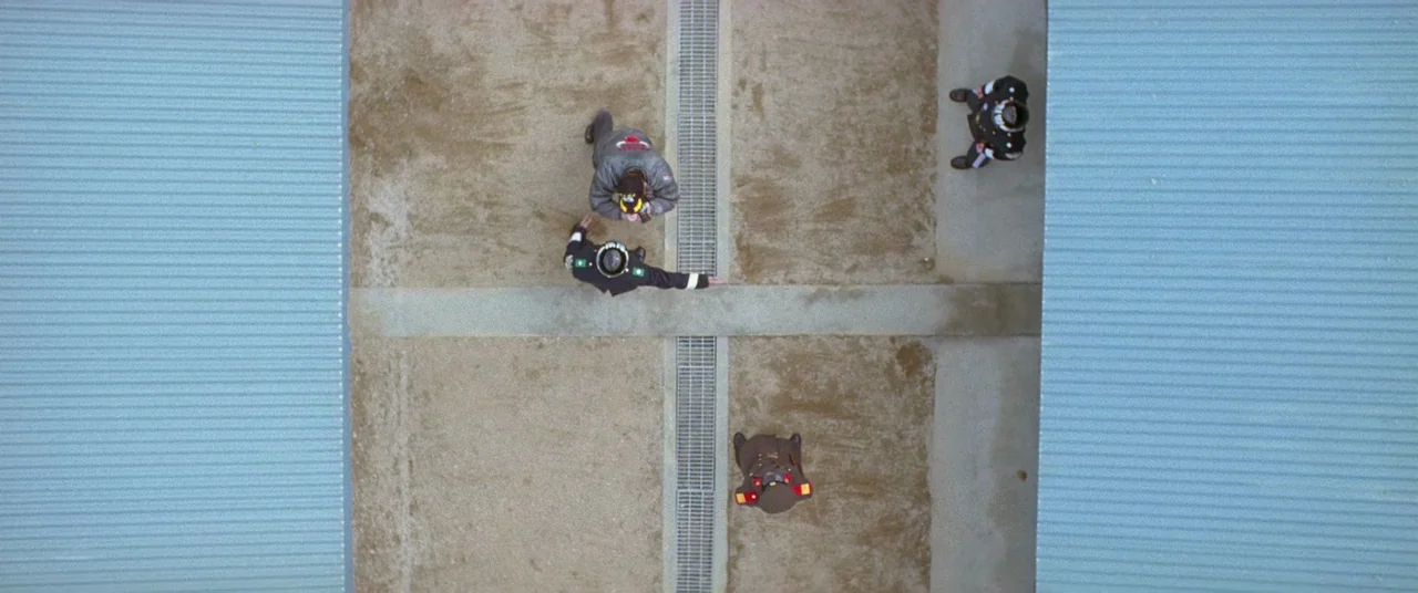 Joint Security Area (2000) movie still: wide — An outdoor military yard with concrete ground and metal drainage grates is flanked by buildings.…