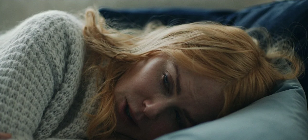 Babygirl (2024) movie still: closeup — A residential bedroom featuring a person resting on a soft blue pillow. The subject lies on their side…