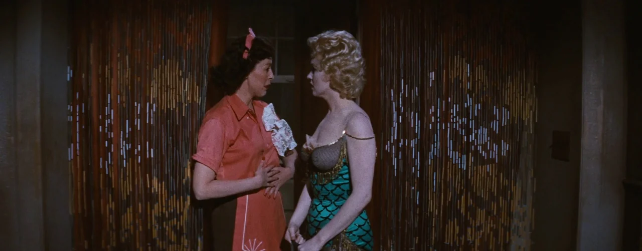 Bus Stop (1956) movie still: medium — A dimly lit room with beaded curtains hanging in the background. Two women stand facing each other in the…