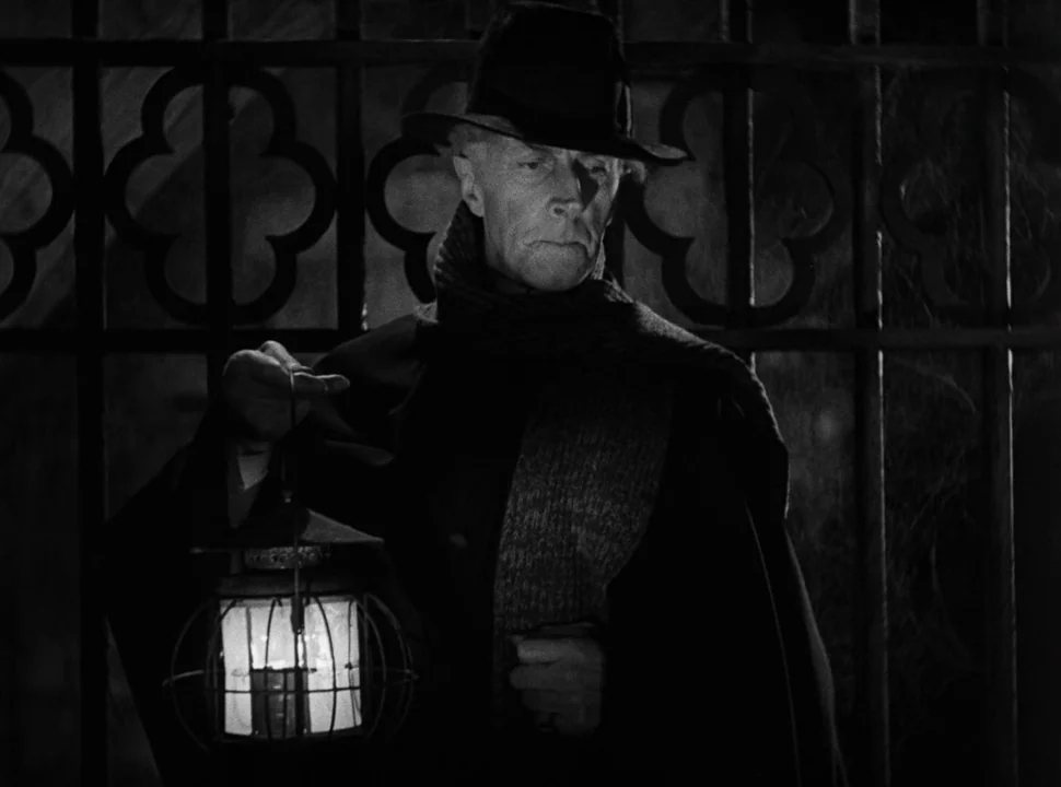 The Bride of Frankenstein (1935) movie still: medium — An elderly man stands at night before a large ornate metal gate. He carries a small metal…