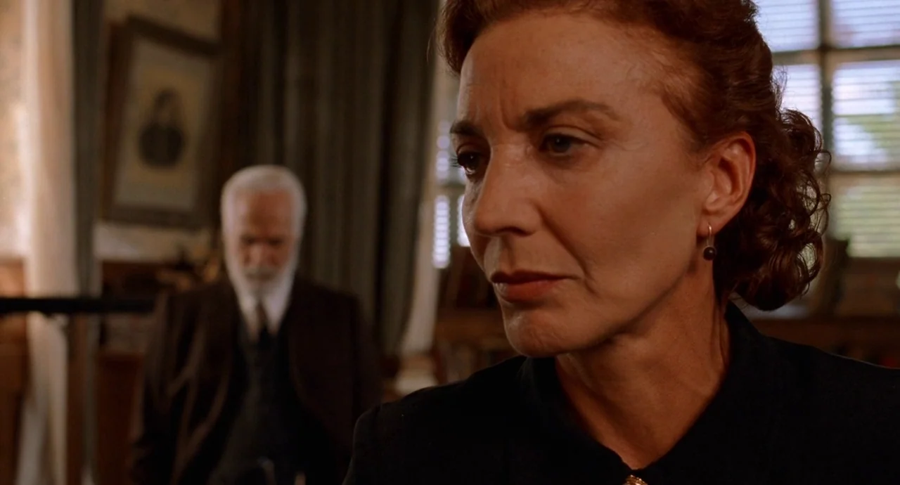 The Devils Backbone (2001) movie still: medium — A dimly lit traditional study features heavy drapes and a portrait hanging on the wall. A woman in…