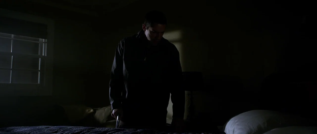 Universal Soldier: Day of Reckoning (2012) movie still: medium — A dark, dimly lit room with a bed positioned near a window. A man stands beside the…