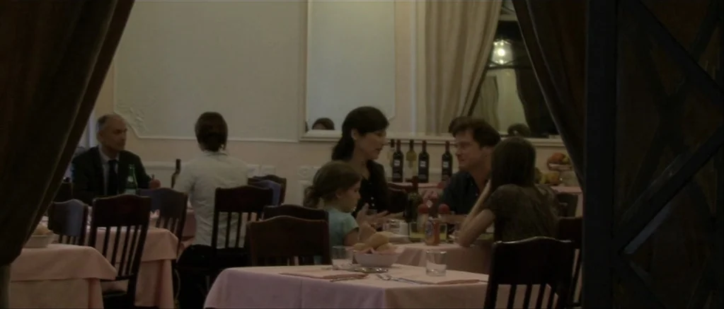 Genova (2008) movie still: wide — A quiet dining room interior features light pink tablecloths and dark wooden chairs. Several patrons sit at…