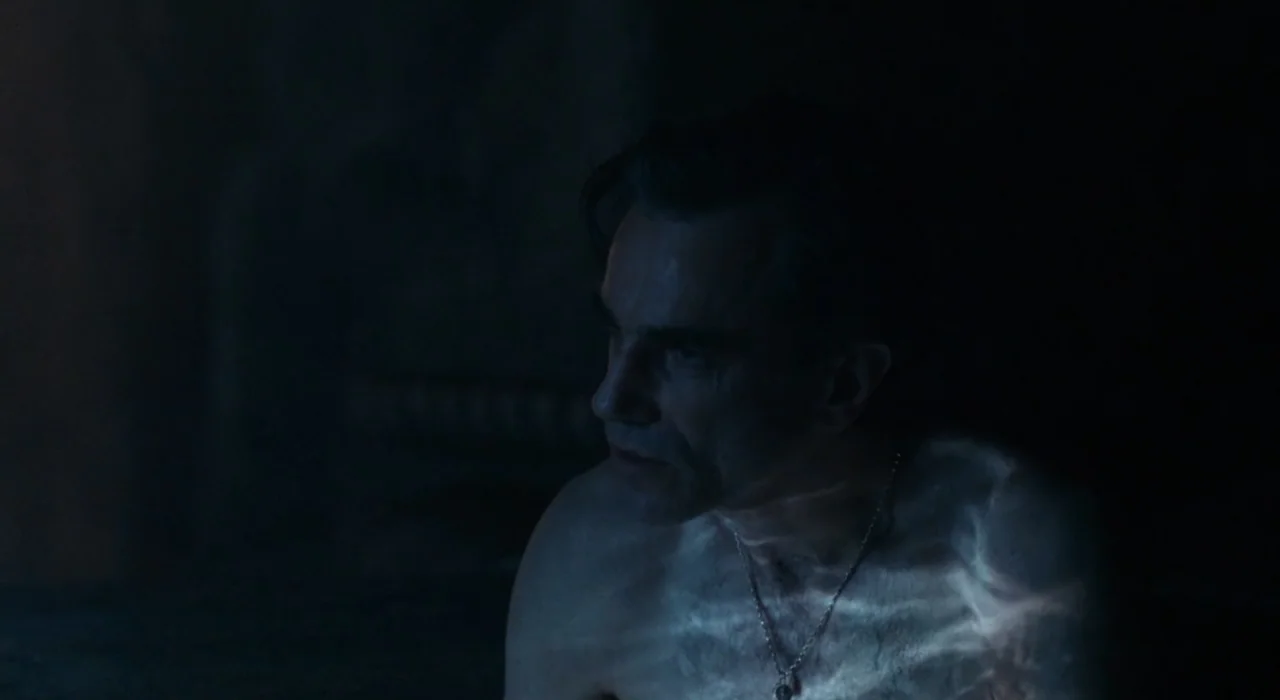 The Great Beauty (2013) movie still: closeup — A dimly lit room at night with deep shadows obscuring the background. A middle-aged man sits…