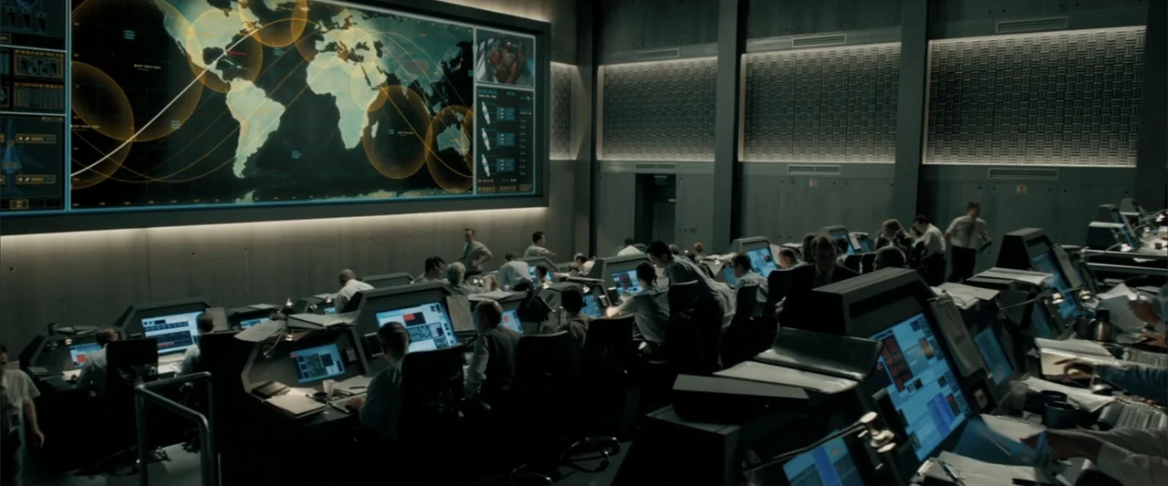 Superman Returns (2006) movie still: wide — A high-tech command center features rows of computer stations and a massive wall display. Many staff…