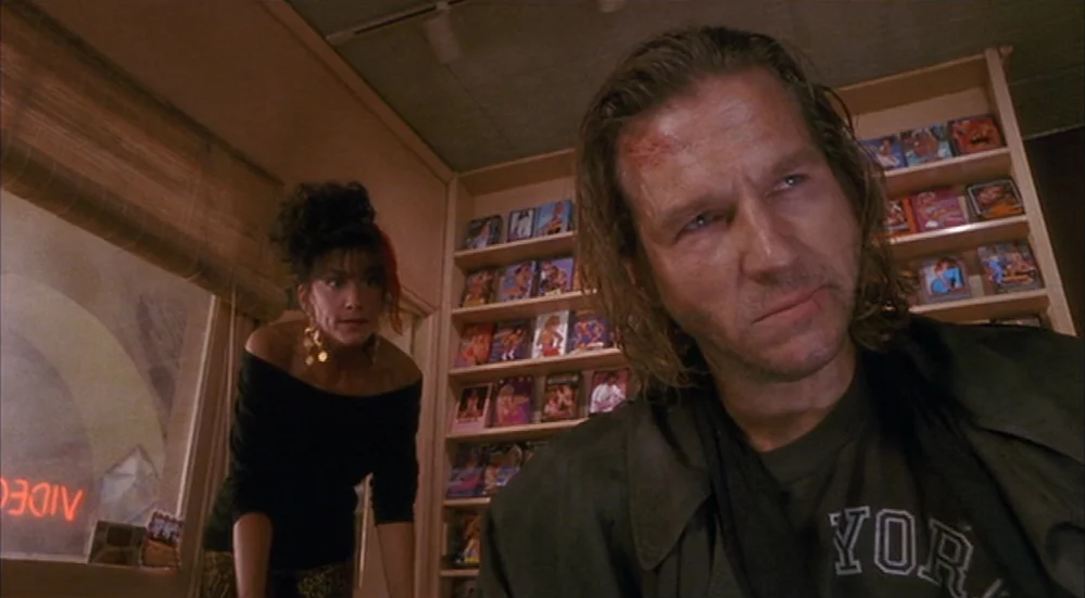 The Fisher King (1991) movie still: medium — A cramped retail space features rows of shelves filled with VHS tapes. A man and woman interact near…
