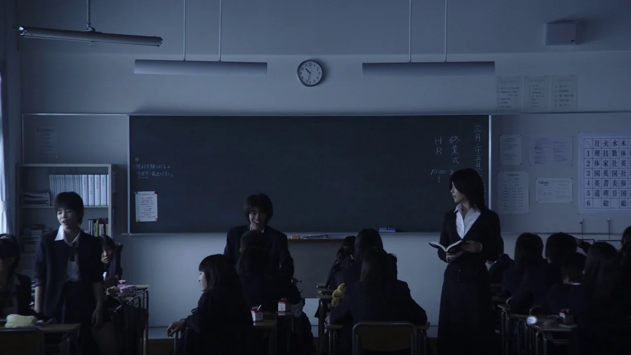 Confessions (2010) movie still: wide — A quiet Japanese classroom with rows of desks and a large green chalkboard. Students occupy the room, with…