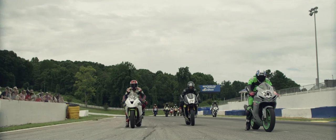 One Fast Move (2024) movie still: wide — A wide view of a professional motorcycle race on an asphalt circuit. Multiple riders in protective suits…