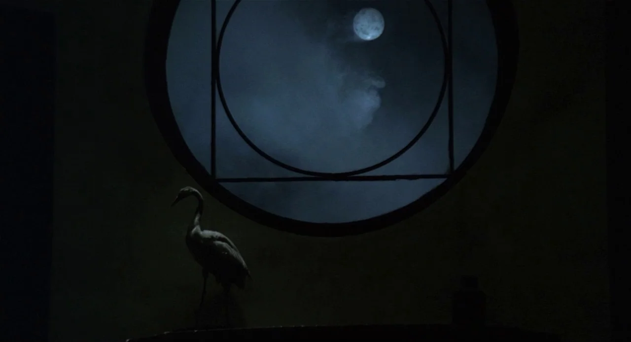 Fellini’s Casanova (1976) movie still: wide — A dark, dimly lit room features a prominent circular window looking out onto the moon. An ornamental…