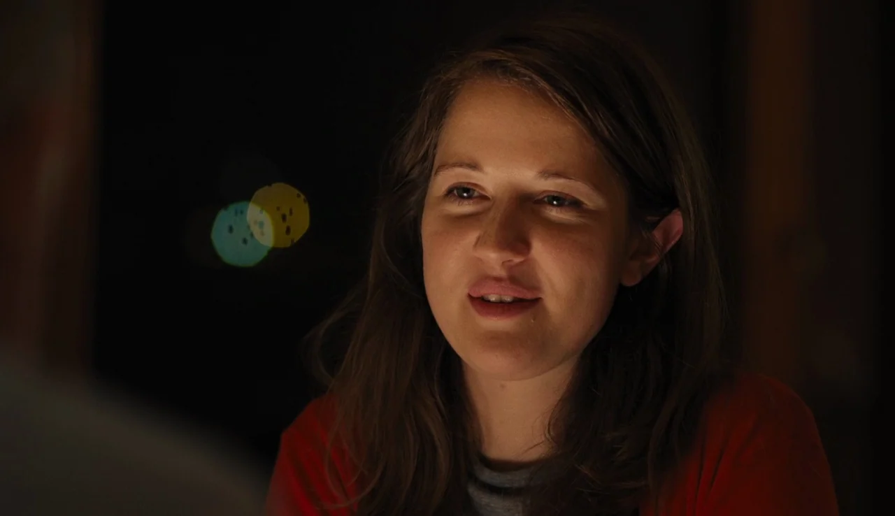 Land Ho! (2014) movie still: closeup — A woman in a red shirt sits in a dimly lit, out-of-focus interior space. She looks off-camera as if engaged…