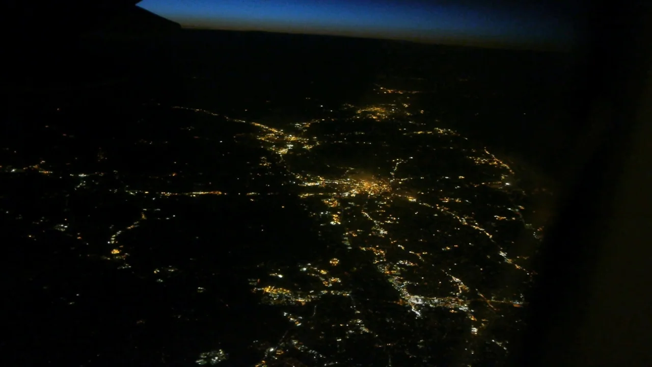 Counting (2015) movie still: establishing — An aerial view of a sprawling landscape during the night from a high altitude. Clusters of golden…