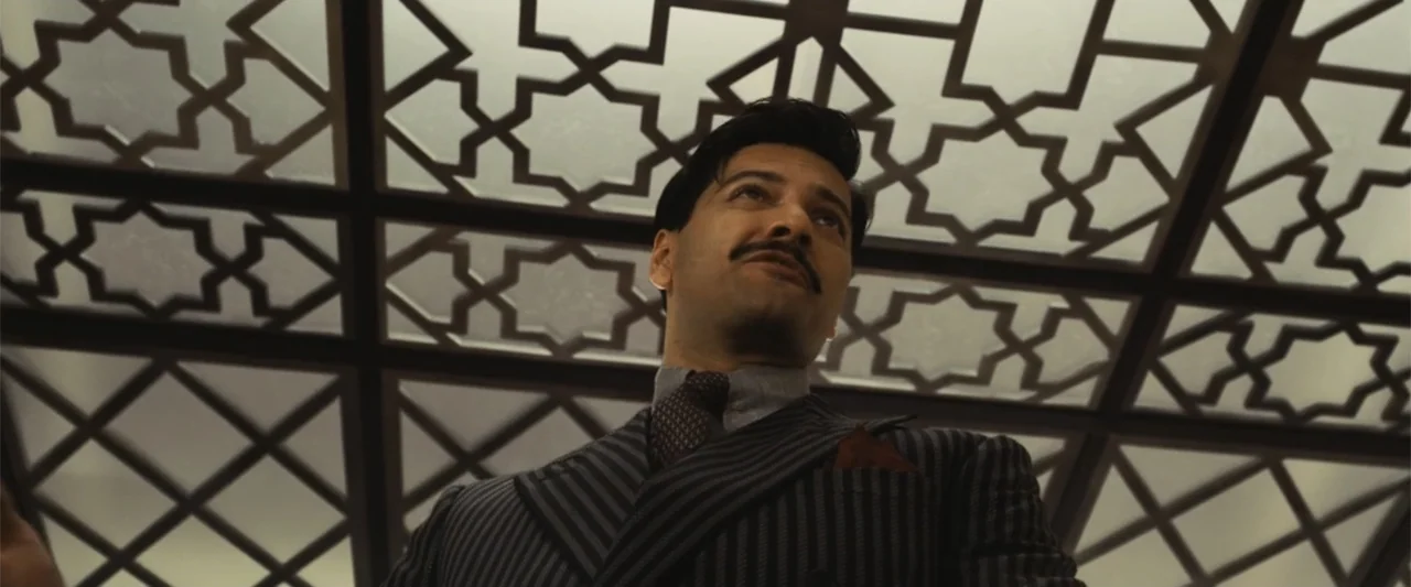 Death on the Nile (2022) movie still: medium — A 1930s style cabin features an overhead light with an intricate geometric patterned frame. A man in…
