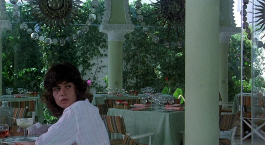 The Passenger (1975) movie still: medium — A patio dining area features green tablecloths, thick columns, and sun-shaped decorative wall mirrors. A…