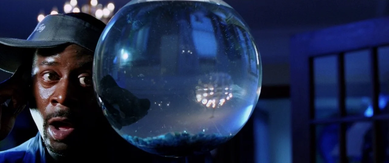 Bad Boys II (2003) movie still: closeup — A dimly lit room at night features a man positioned near a glass bowl. The man looks through the round…