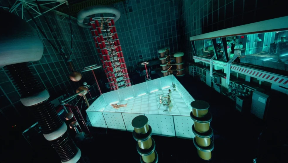 The Zero Theorem (2013) movie still: wide — A vast, dark industrial high-voltage testing facility contains a large, glowing central glass box.…
