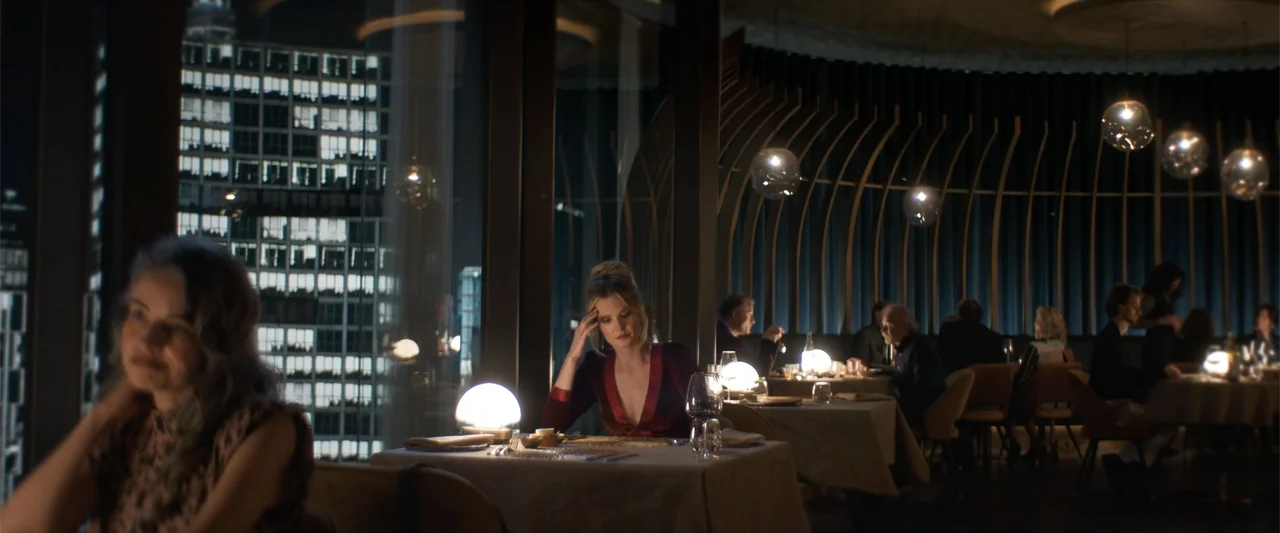 Drop (2025) movie still: medium — A dimly lit upscale restaurant features rows of tables with spherical table lamps. A woman in a burgundy dress…