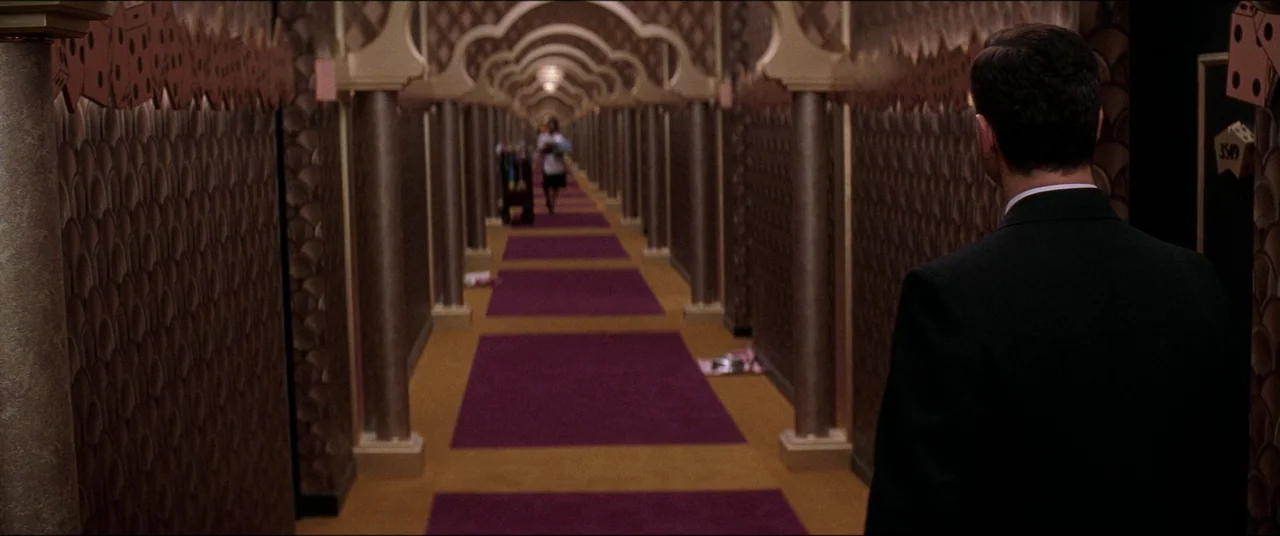 Snake Eyes (1998) movie still: medium — A long, ornate hotel corridor features patterned wallpaper and an arched architectural motif. A man in a…
