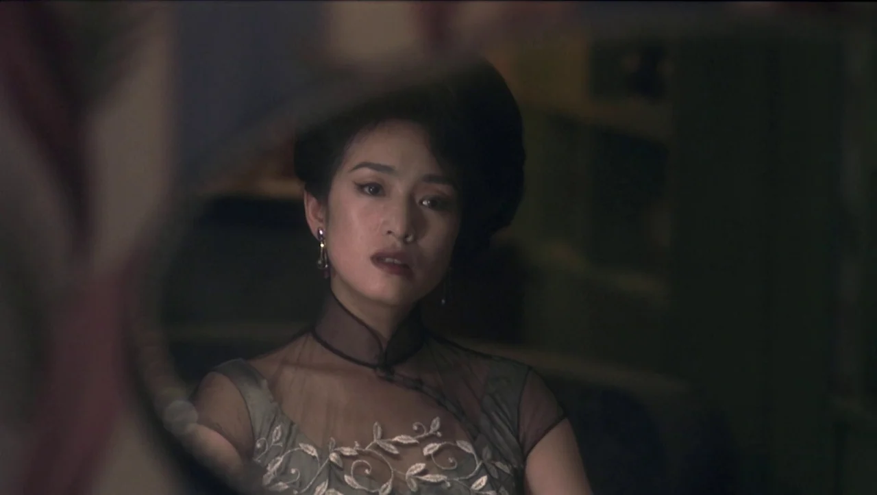 Eros (2004) movie still: closeup — A woman looks into a vanity mirror in a dim interior setting. The frame is obscured by the circular edge of the…