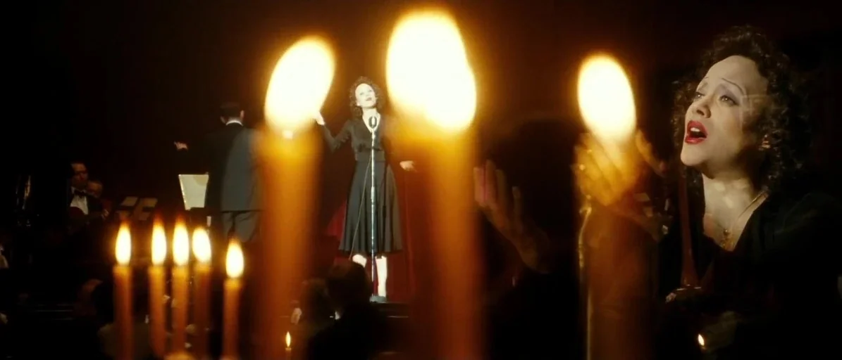 La Vie En Rose (2007) movie still: medium — An dimly lit concert stage features a female singer standing by a central microphone. She performs while…
