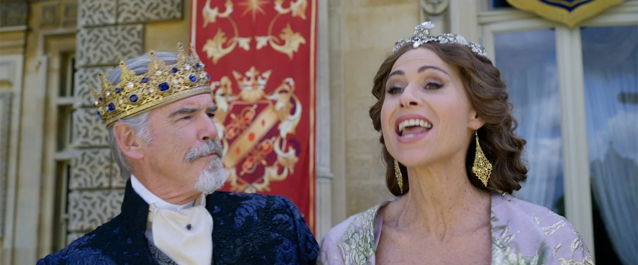 Cinderella (2015) movie still: medium — An outdoor palace courtyard features a stone wall with a large red royal banner hanging. A king and queen in…