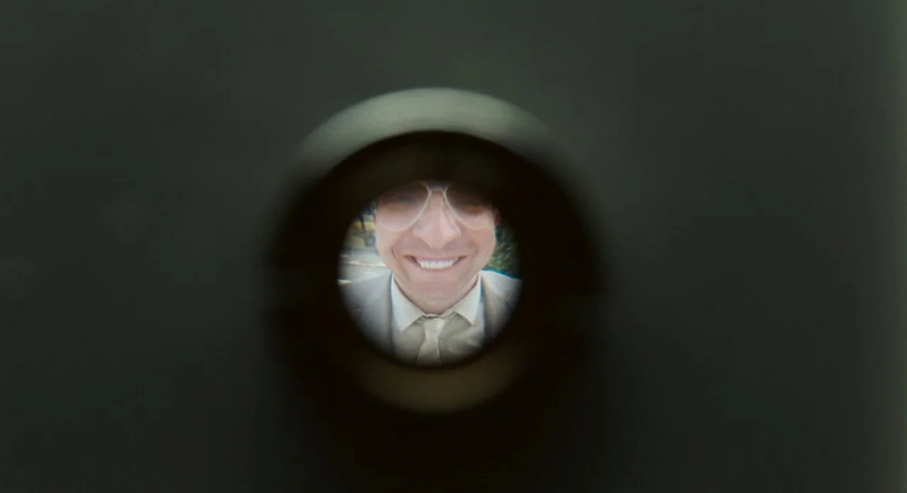 London Boulevard (2010) movie still: closeup — A view through a metal peephole reveals a man standing on a porch. The man faces the camera directly…