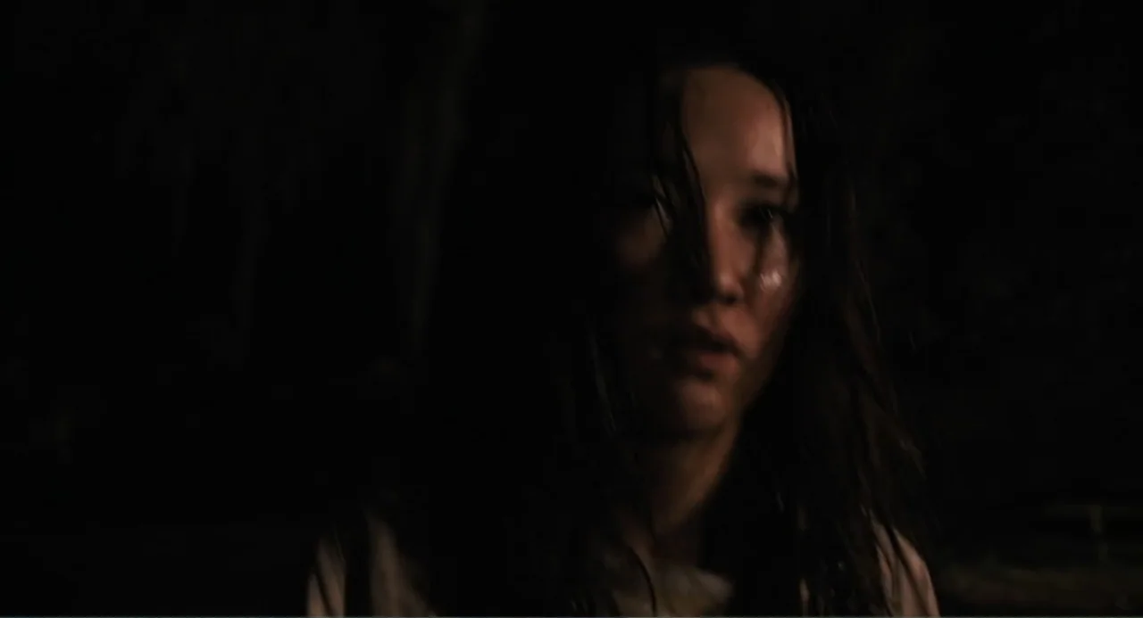 Mona Lisa and the Blood Moon (2022) movie still: closeup — A woman stands in a dark wooded area at night. She looks forward while her hair appears…