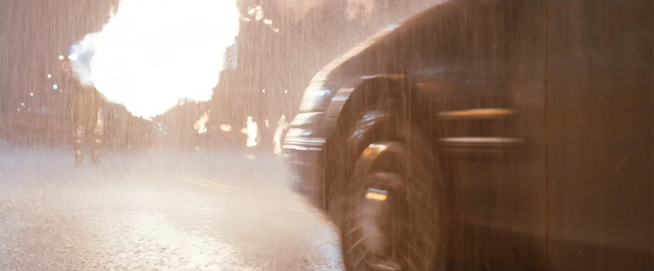 Lethal Weapon 4 (1998) movie still: medium — A dark car speeds across a wet asphalt road during a heavy rainstorm. A bright explosion of light…