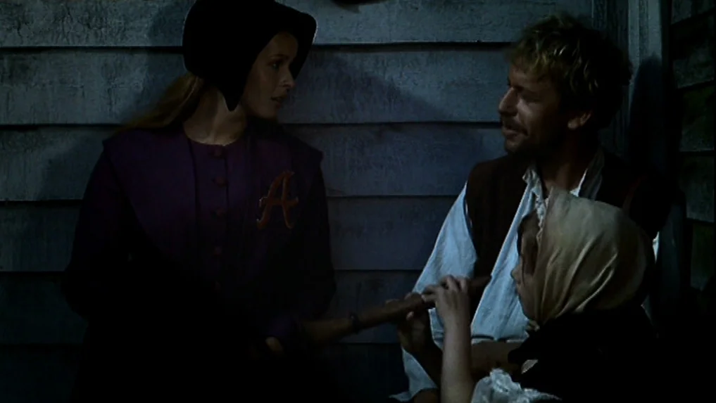 The Scarlet Letter (1973) movie still: medium — A wooden siding wall forms the backdrop for three people on a porch at night. The woman and man…