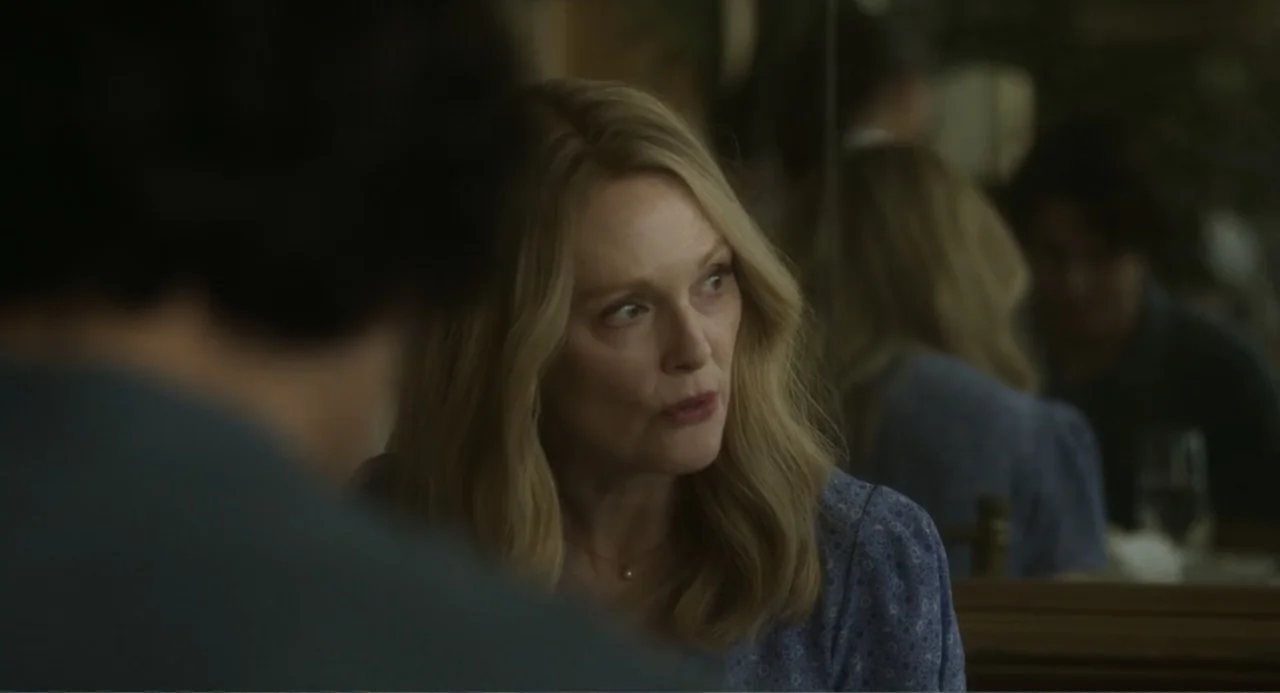 May December (2023) movie still: closeup — A restaurant table with a woman engaged in conversation with an out-of-focus subject. The background…